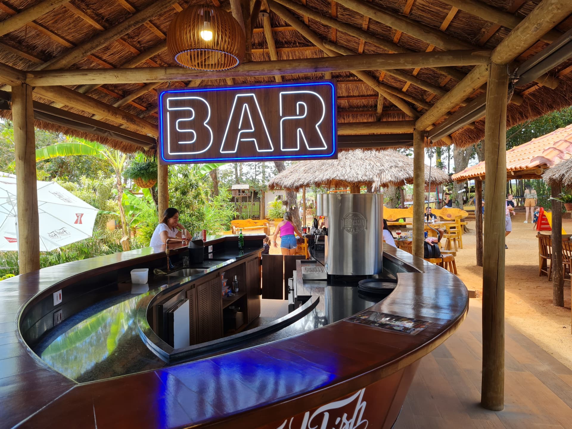 Balcão curvo do bar-barco com atendimento e chopeira, cercado pelo jardim