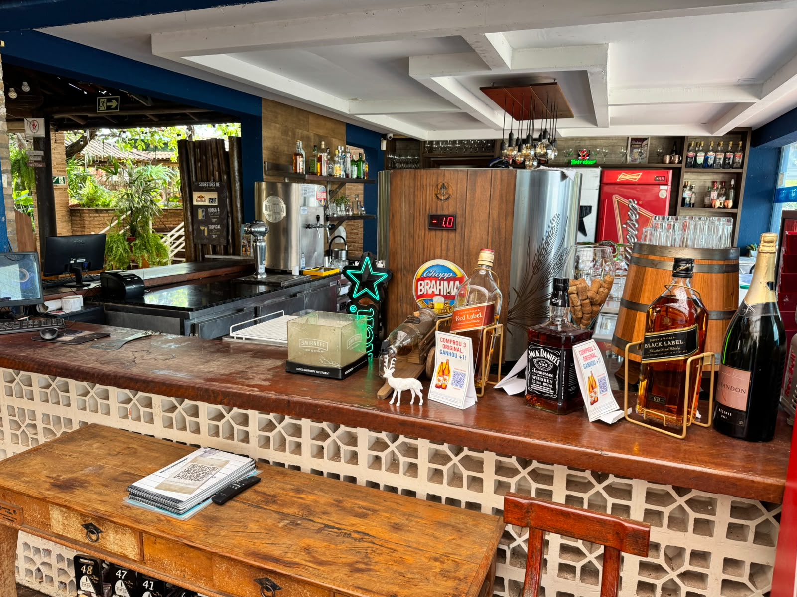 Balcão interno do bar com tampo de madeira, cobogós, chopeira Brahma e vista para o jardim