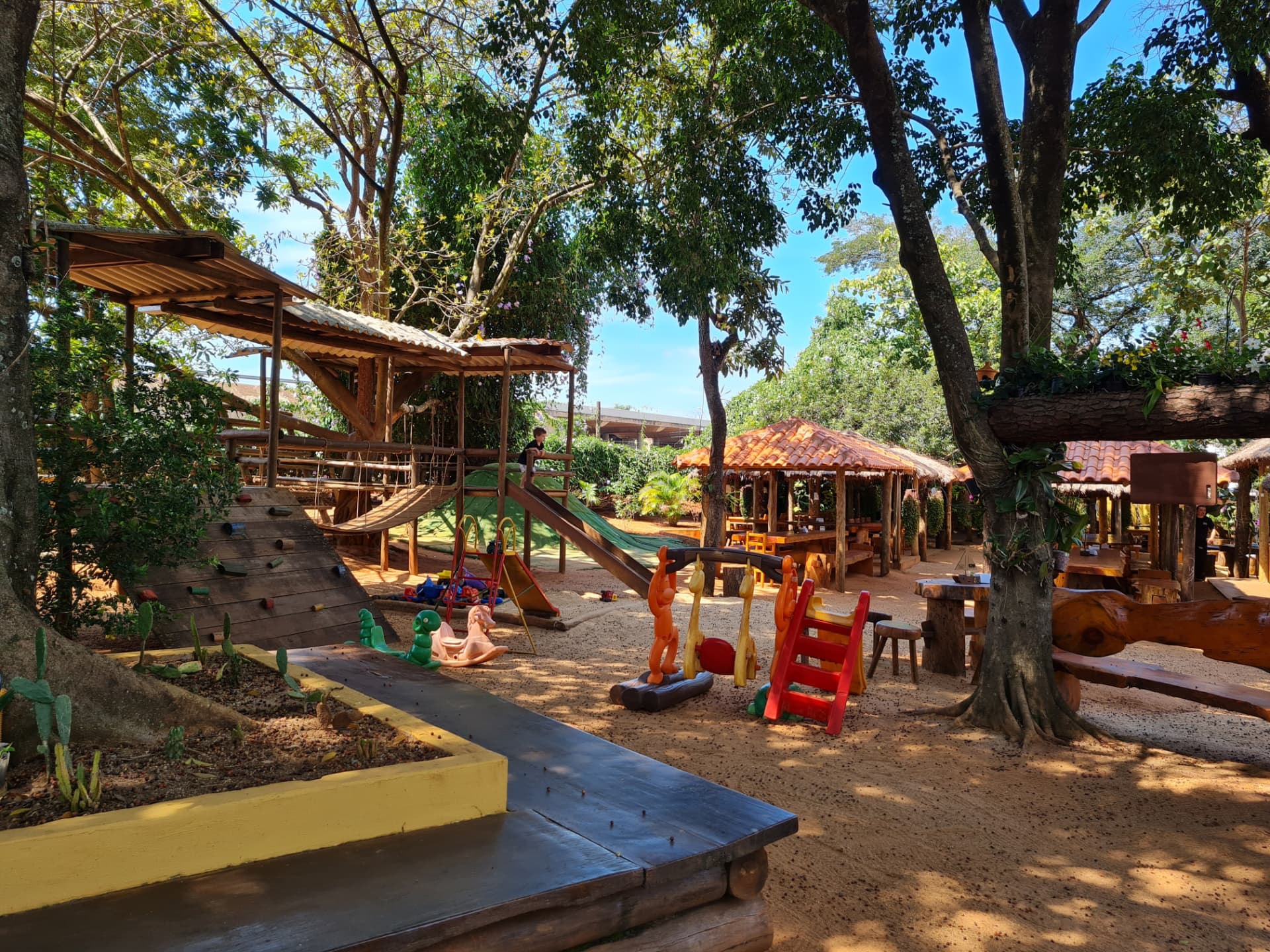 Playground de madeira com casa na árvore, escorregador e brinquedos sob árvores altas