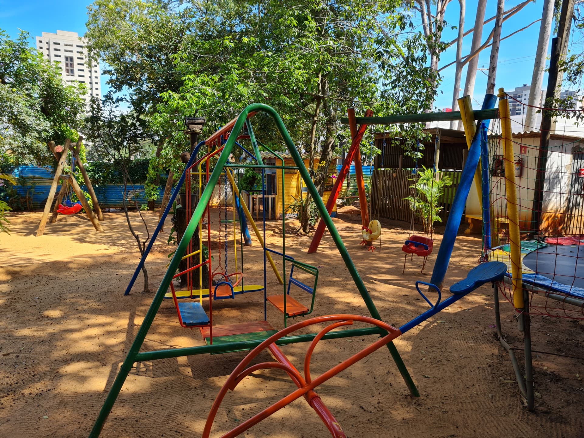 Conjunto de balanços coloridos com cadeirinhas para bebês e cama elástica ao fundo