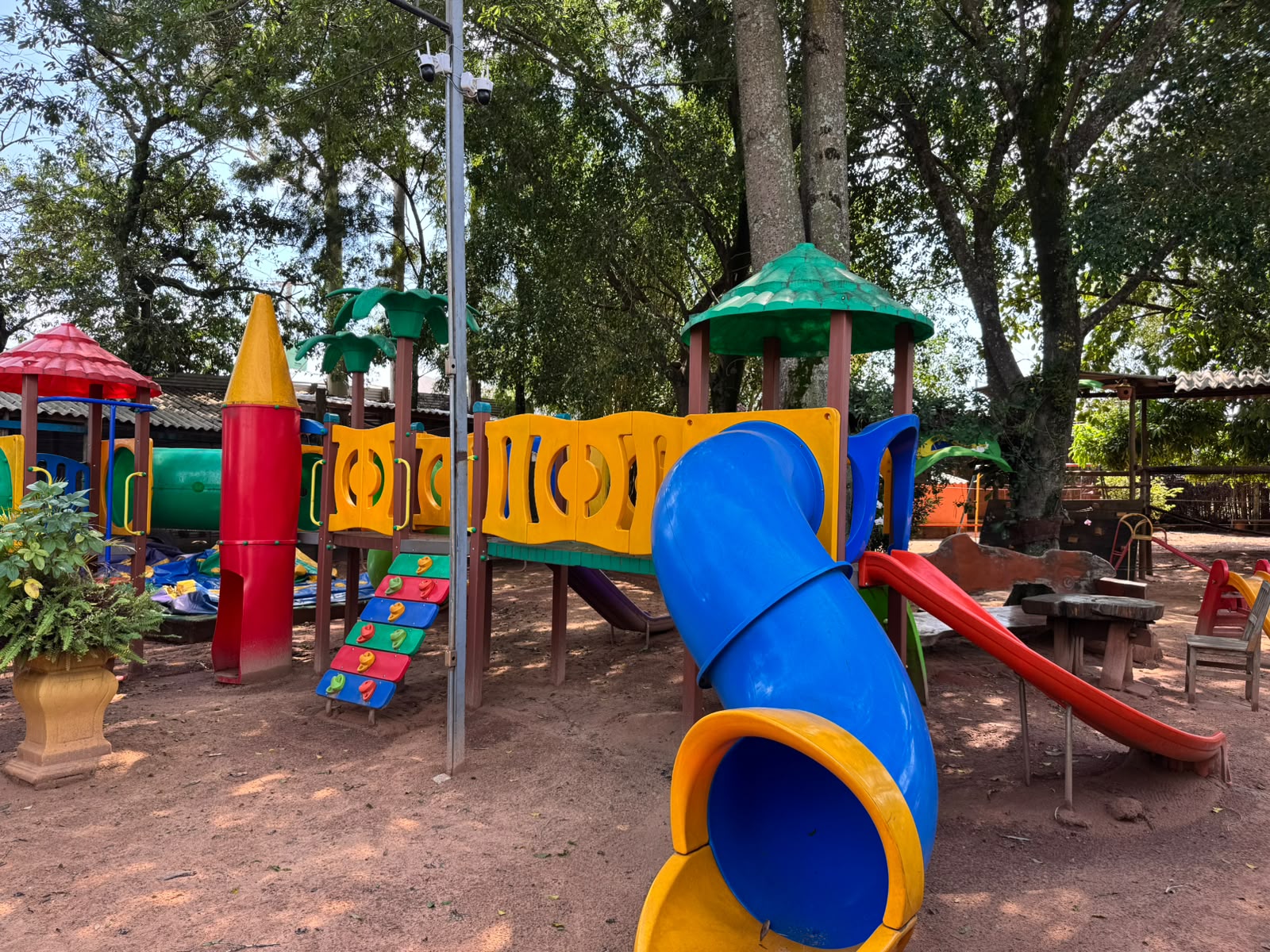 Playground ao ar livre com torre foguete, escorregador azul e mesas de madeira