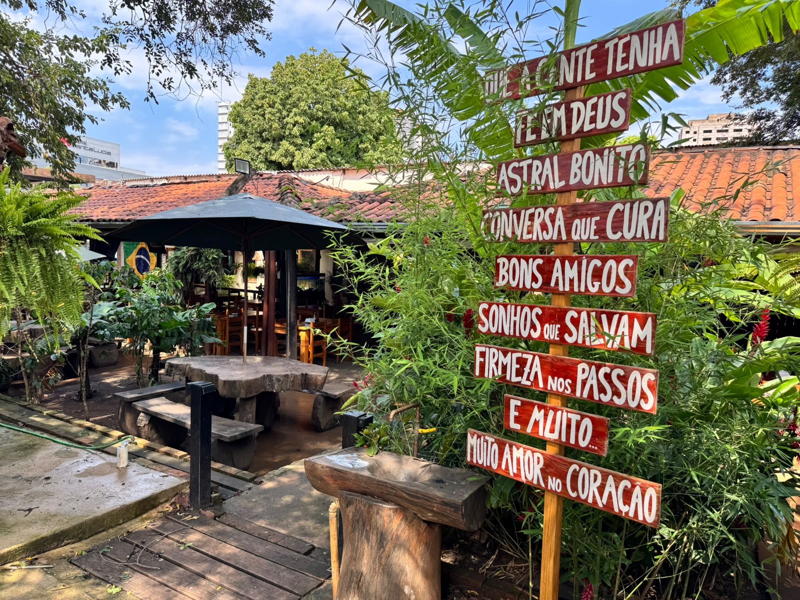 Área externa com mesas de madeira rústica e totem decorativo com mensagens sob o verde